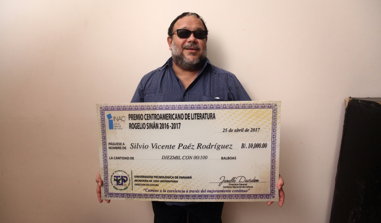 El escritor Héctor Collado, quien leyó el fallo, muestra el cheque a que se hizo acreedor el ganador. /Foto Aurelio Herrera Suira.