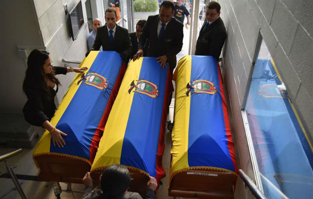 Un grupo de personas coloca banderas de Ecuador sobre los féretros. Foto: EFE