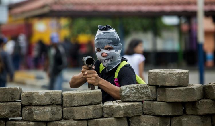 Un joven con la cara tapada y un lanza morteros cuida una barricada en el barrio indígena de Monimbó. EFE