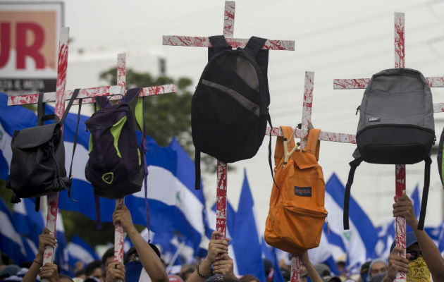 Varios jóvenes con unas cruces con mochilas en honor a los estudiantes que murieron en las pasadas manifestaciones. FOTO/EFE