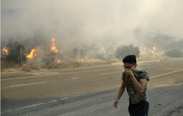 Un joven camina cubriéndose la nariz del humo causado por el fuego en Santa Clarita. Foto: AP.  