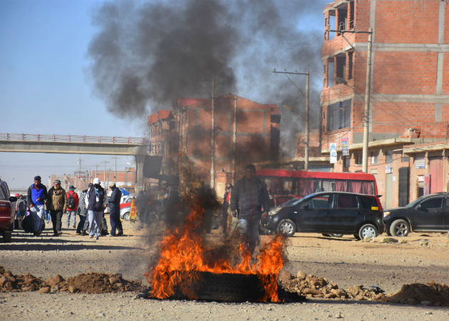 Un hombre cruza un bloqueo de una carretera durante las protestas en Cochabamba. Fotos: EFE.