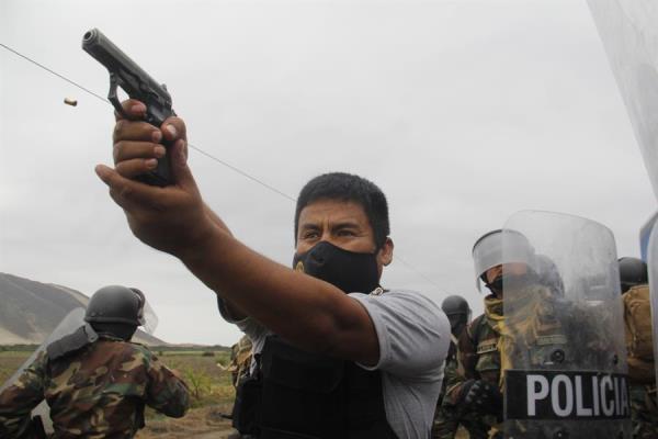 Un miembro de la Policía mientras apunta su arma a manifestantes durante una protesta de trabajadores agroindustriales 