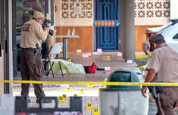 Un oficial de policía fotografía el cuerpo de una de las víctimas del tiroteo registrado en la entrada del salón de banquetes Billiards en Miami Gardens, Florida, Estados Unidos, este 30 de mayo. 