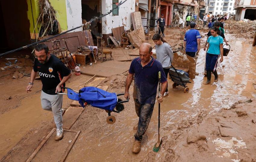 Vecinos cruzan una calle llena de fango y escombros en la localidad de Paiporta este sábado tras el paso de la DANA. Foto: EFE