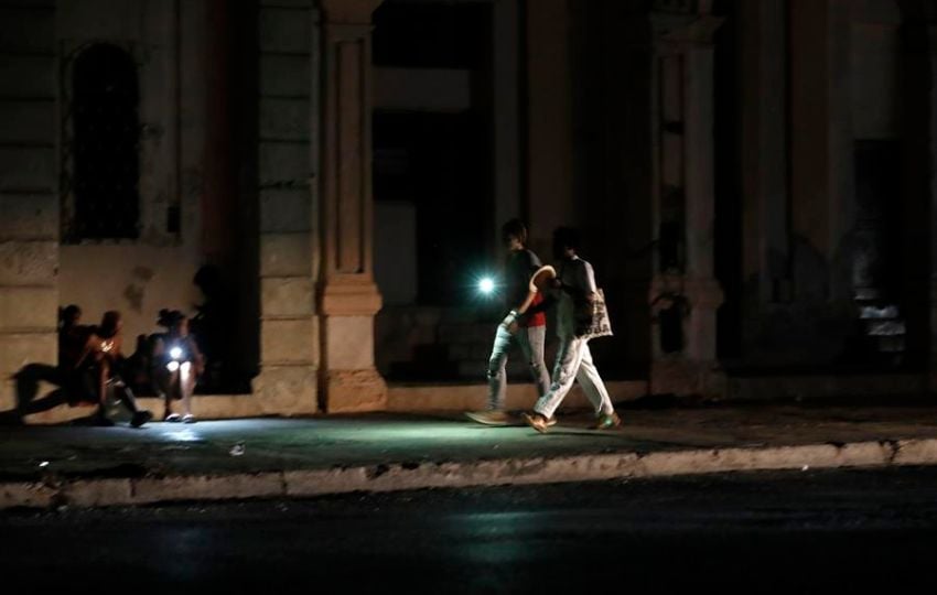 Personas caminan por una calle sin iluminación auxiliándose con la luz de su celular durante un apagón. Foto: EFE