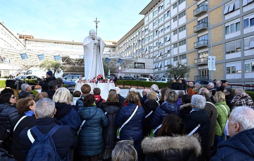 Fieles rezan por el papa Francisco ante la estatua del Papa San Juan Pablo II. Foto: EFE