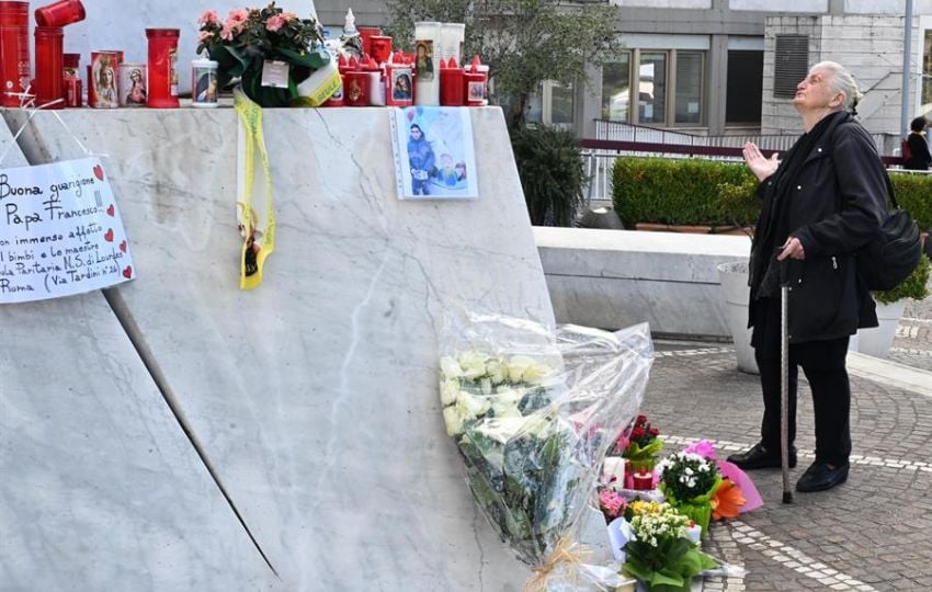 Una mujer reza bajo una estatua del Papa San Juan Pablo II en las afueras del Hospital Universitario Gemelli. Foto: EFE