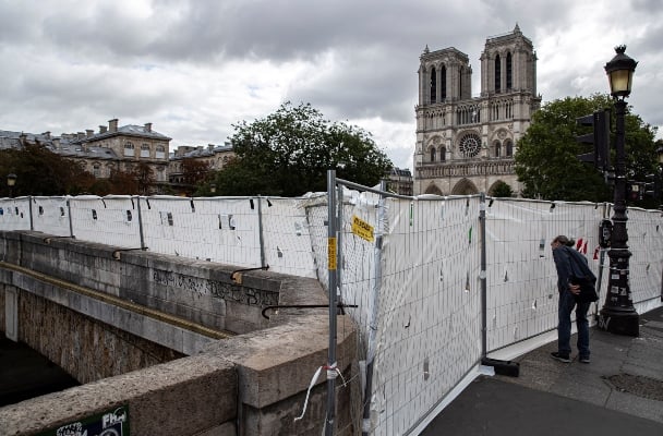 Los turistas miran a través de paneles de protección que aseguran un perímetro alrededor de la Catedral de Notre Dame antes del inicio de un tratamiento masivo de descontaminación de plomo alrededor del monumento, en París.FOTO/AP